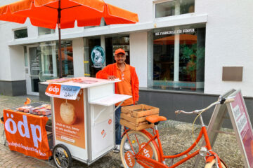 Der Kempener ÖDP-Spitzenkandidat Jeyaratnam Caniceus bei einem Infostand mit orangem Fahrrad. Foto: Prof. Dr. Herbert Einsiedler