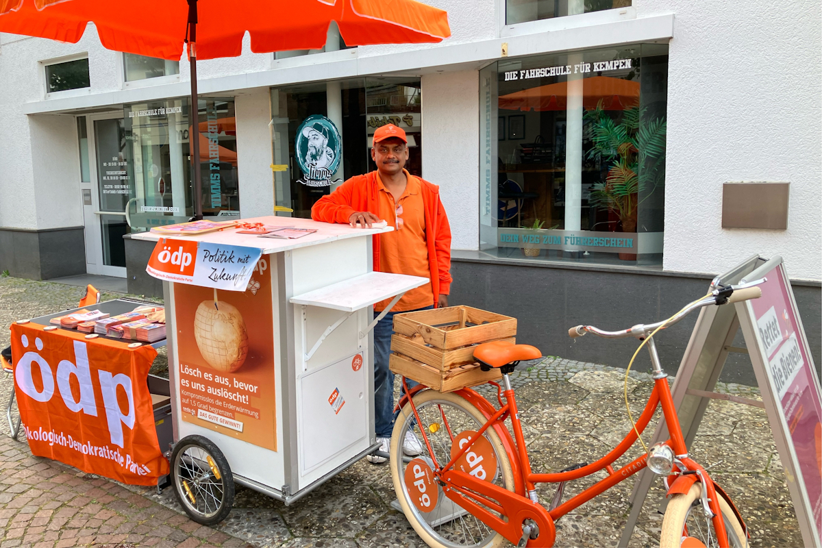 Der Kempener ÖDP-Spitzenkandidat Jeyaratnam Caniceus bei einem Infostand mit orangem Fahrrad. Foto: Prof. Dr. Herbert Einsiedler