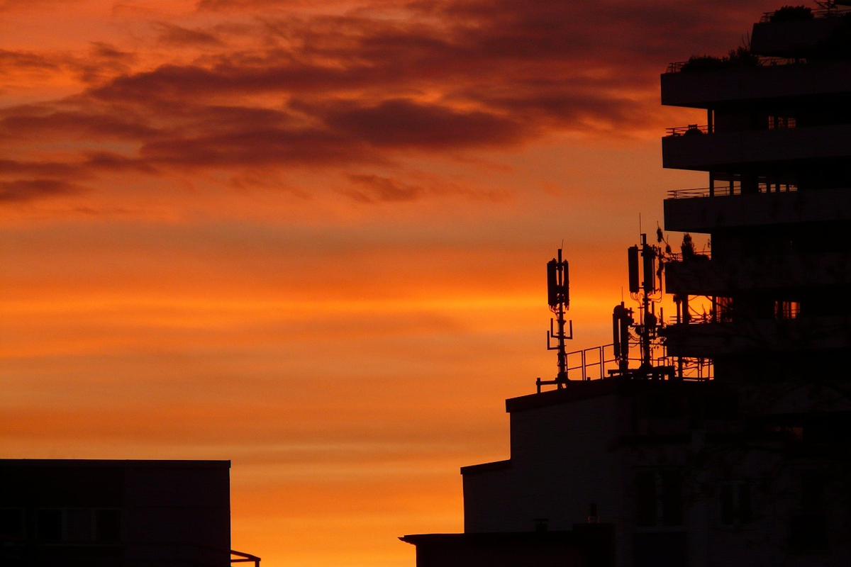 Auf dem Dach eines Wohnhauses stehen mehrere Mobilfunk-Antennen. Der Himmel im Hintergrund ist in ein kräftiges Abendrot getaucht. Foto: Hans / pixabay.com