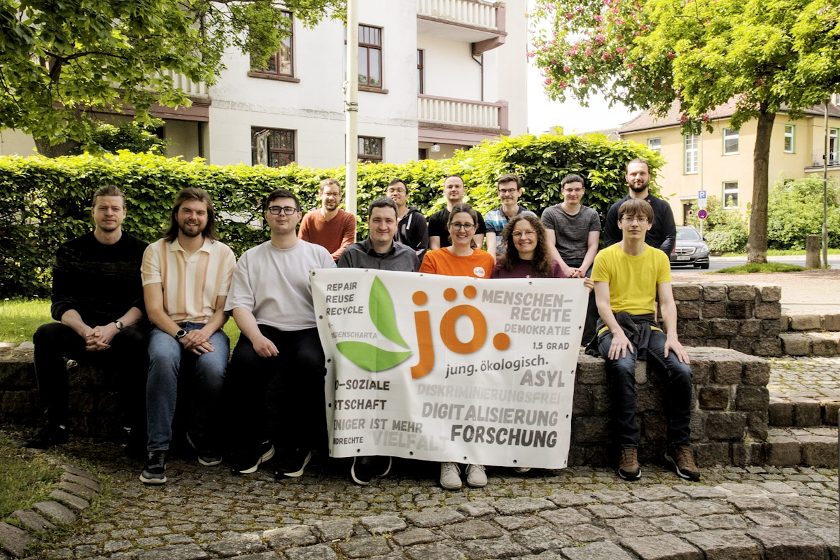 Gruppenbild von JÖ-Mitgliedern der Bundesversammlung 2026. Sie sitzen in einer Grünanlage in Kassel auf Steinstufen. Die vordere Reihe hält die Fahne der JÖ vor sich. Foto: Helmut Kauer